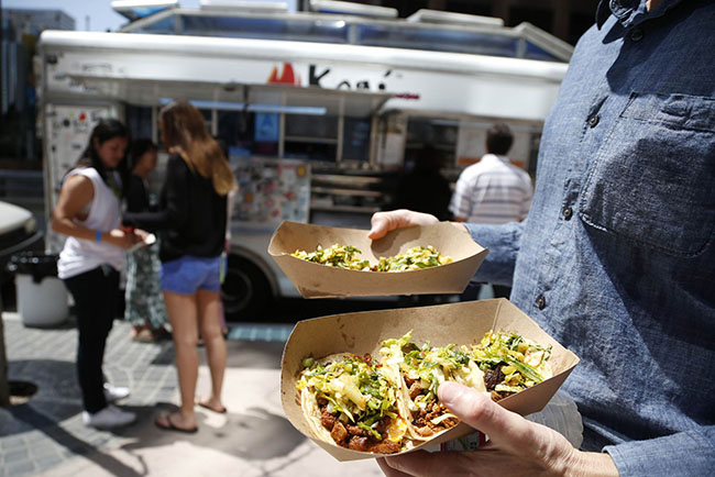 People buy food from the Kogi truck in Los Angeles, California, June 6, 2014. Kogi Korean BBQ, a Korean taco truck that tweeted its way to international stardom in 2008, is the ultimate example of L.A.'s vibrant food culture. It was the brainchild of chef Roy Choi, who was a toddler when his family immigrated to the United States from Korea and is now famous for launching the hipster food truck trend that took the United States by storm. REUTERS/Lucy Nicholson (UNITED STATES - Tags: SOCIETY FOOD)
